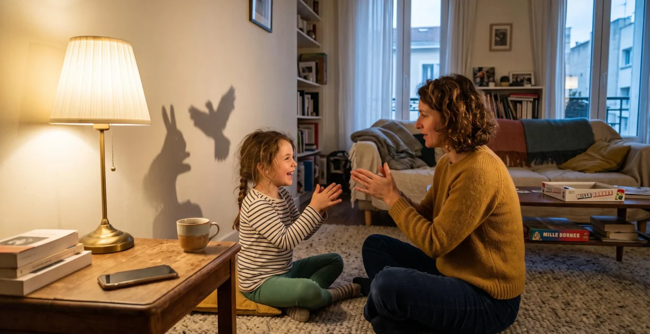 Un parent et un enfant jouent ensemble à des ombres chinoises sur le mur d'un salon, dans la lumière d'une lampe, le téléphone posé à l'écart.
